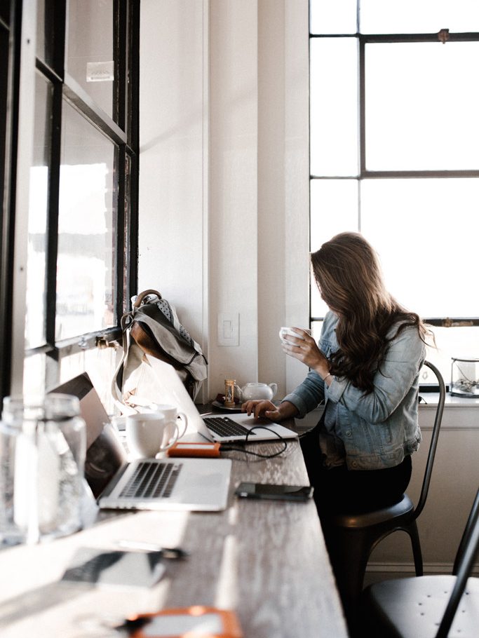 Créatrice digitale dans un coworking boit un café assise devant son ordinateur.