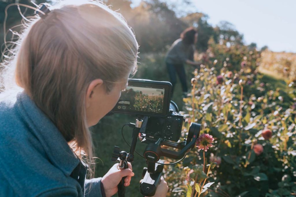 Jeune femme vidéaste filme en extérieur un reportage vidéo corporate.