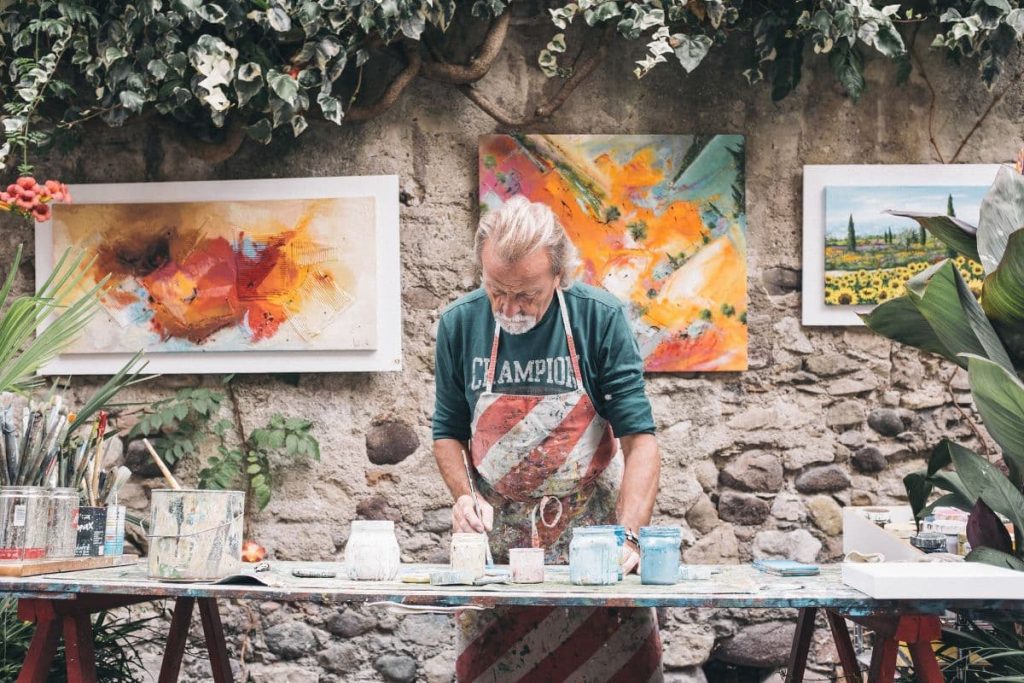 Artiste peintre en tablier occupé de mélanger des couleurs sur une table en bois.