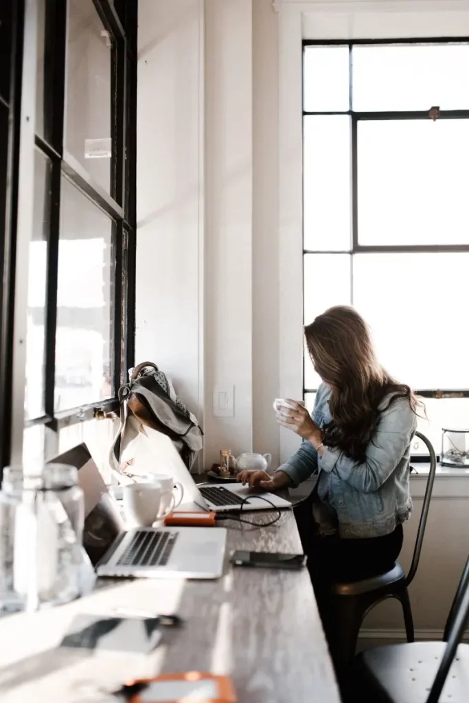 Une femme assise au bureau devant son ordinateur, un mug de café en main.