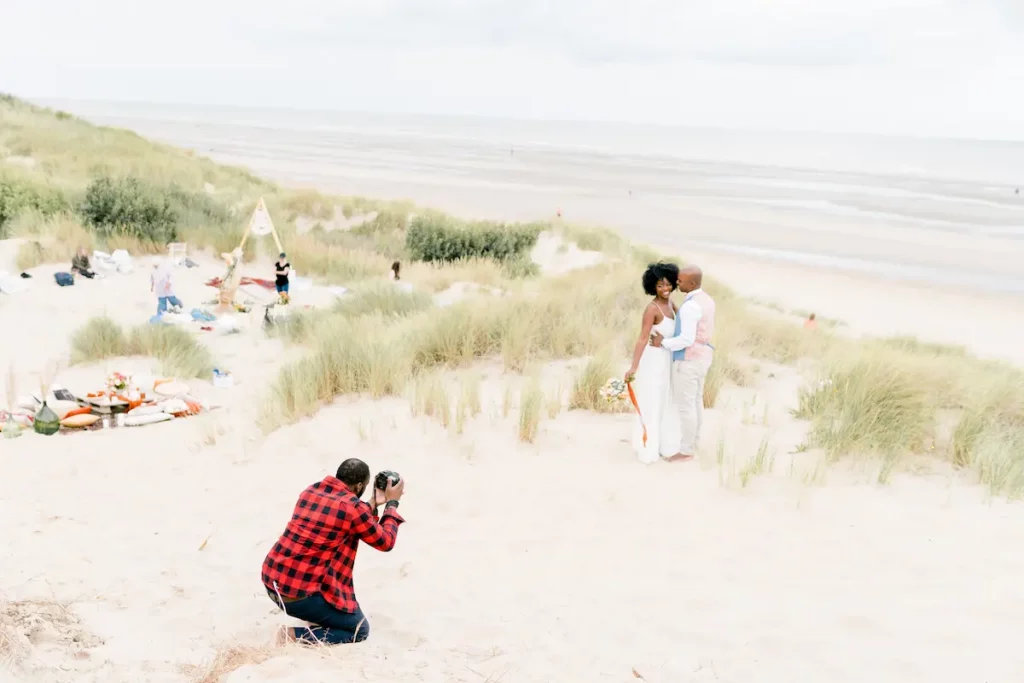 Photographe qui dirige un couple de jeunes mariés pendant une séance photo à la mer du Nord.
